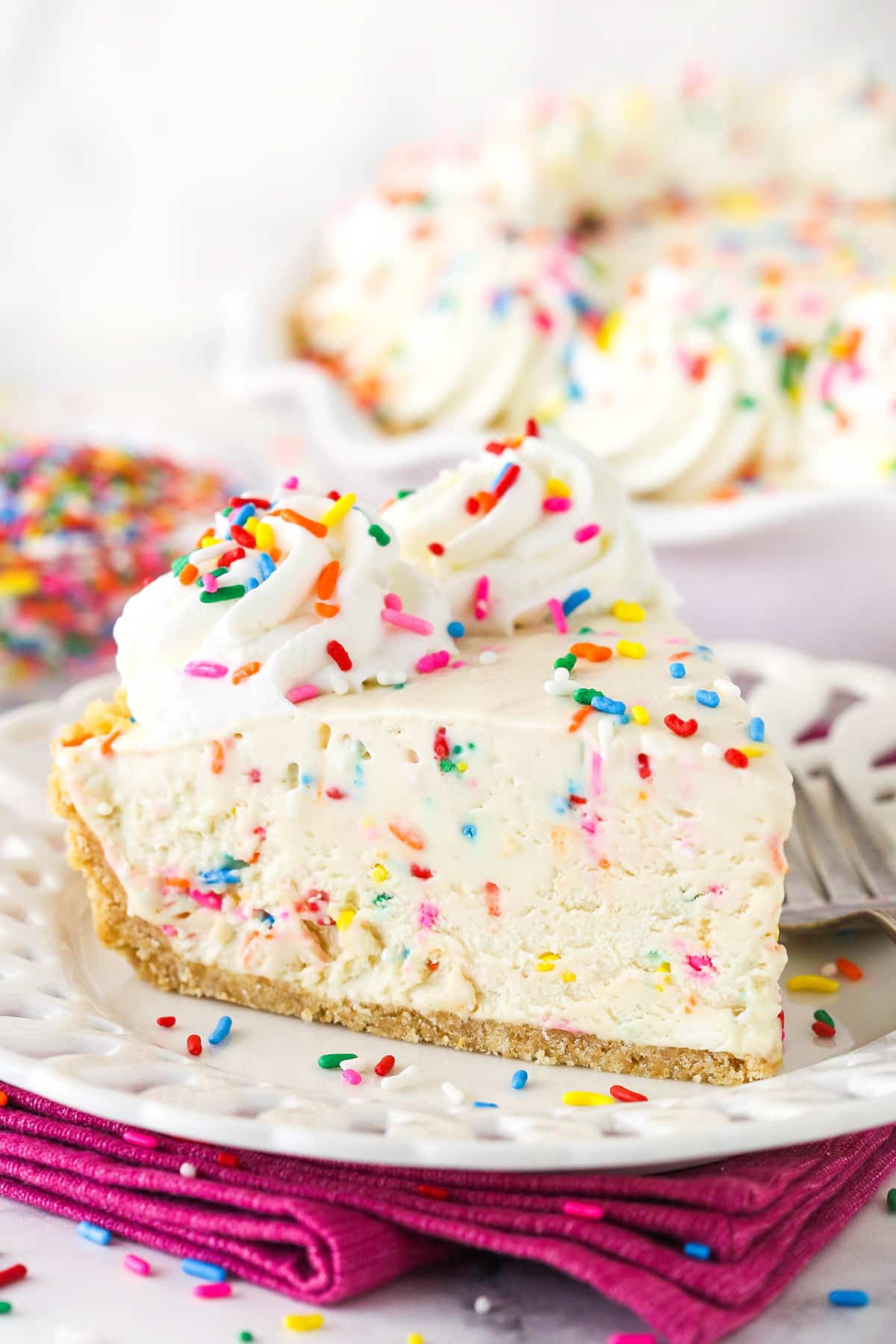slice of cake batter ice cream pie on white plate with bright pink napkin and sprinkles in background