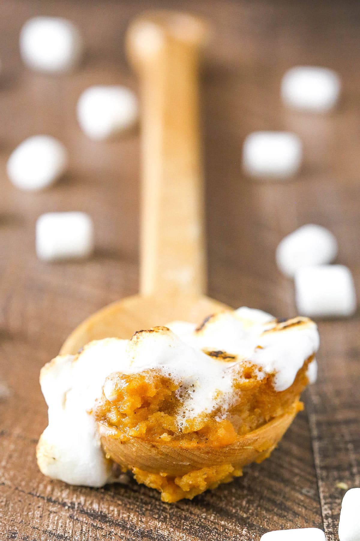 A wooden spoon with sweet potato casserole and marshmallows in it.