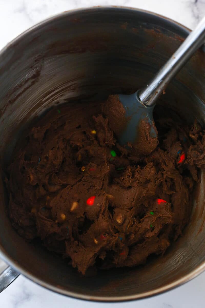 A spatula stirring M&Ms into chocolate cookie dough