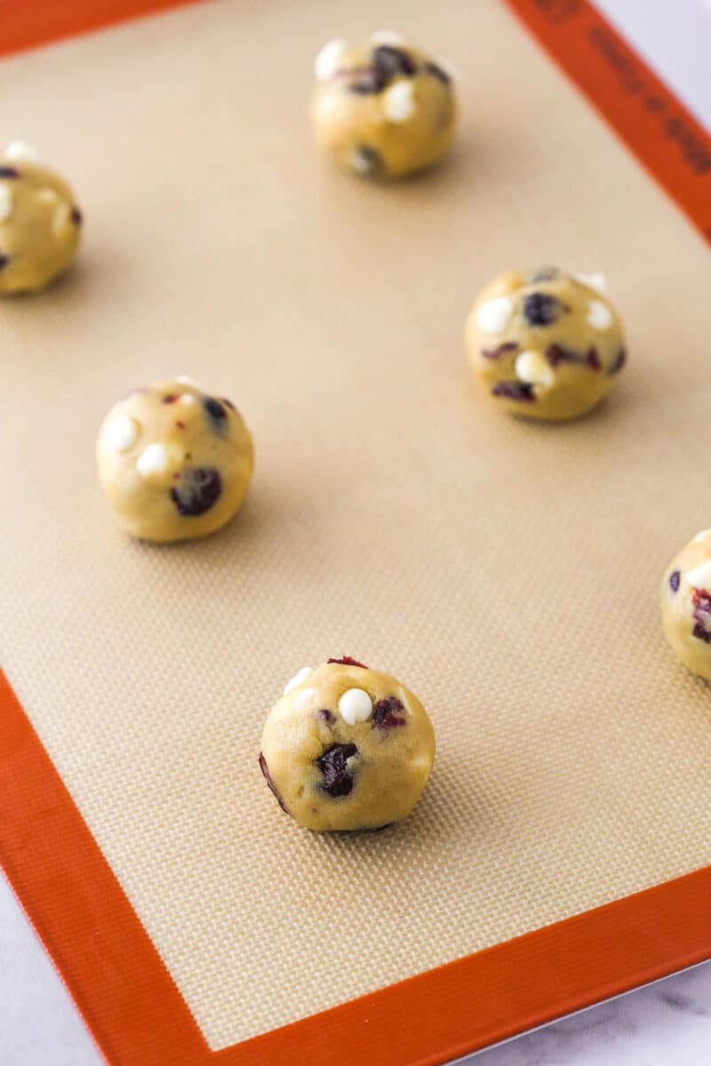 Balls of cranberry white chocolate chip cookie dough on a baking sheet