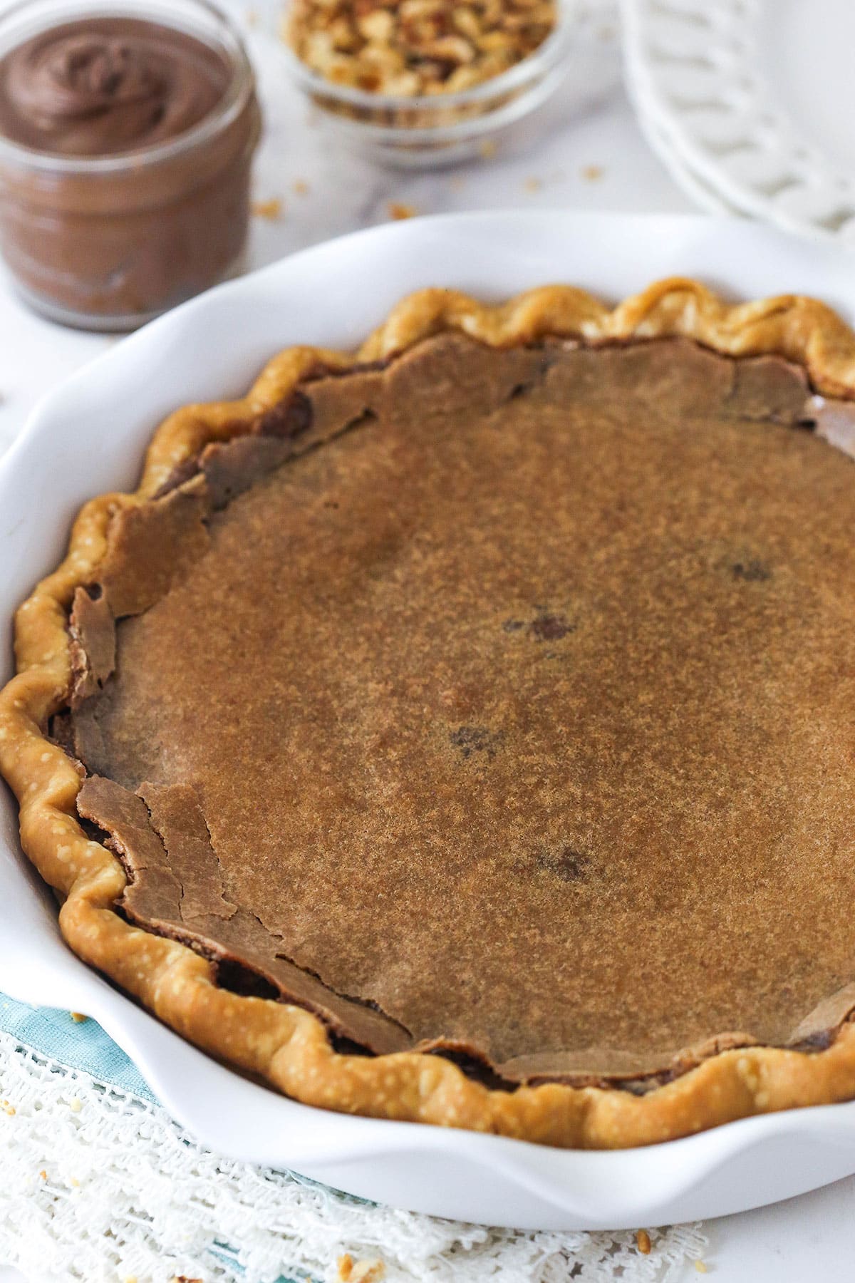 chocolate hazelnut chess pie in white pie dish with Nutella and hazelnuts in the background