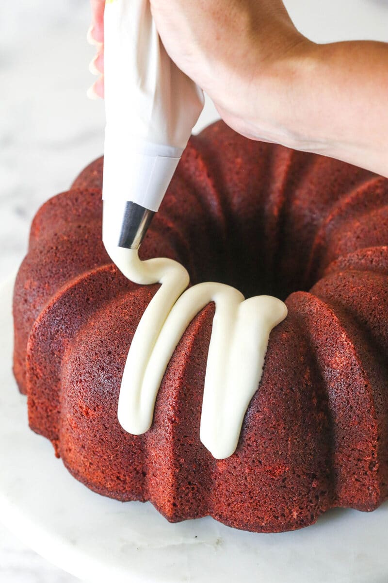 Drizzling cream cheese frosting over red velvet cheesecake bundt cake