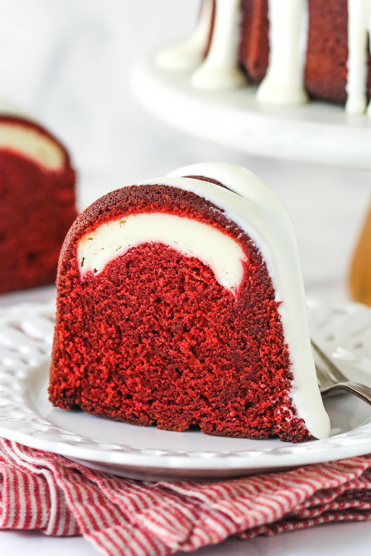 A slice of red velvet cheesecake swirl bundt cake on a white plate