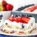 slice of berry icebox cake on white plate with blue napkin underneath and berries in the background