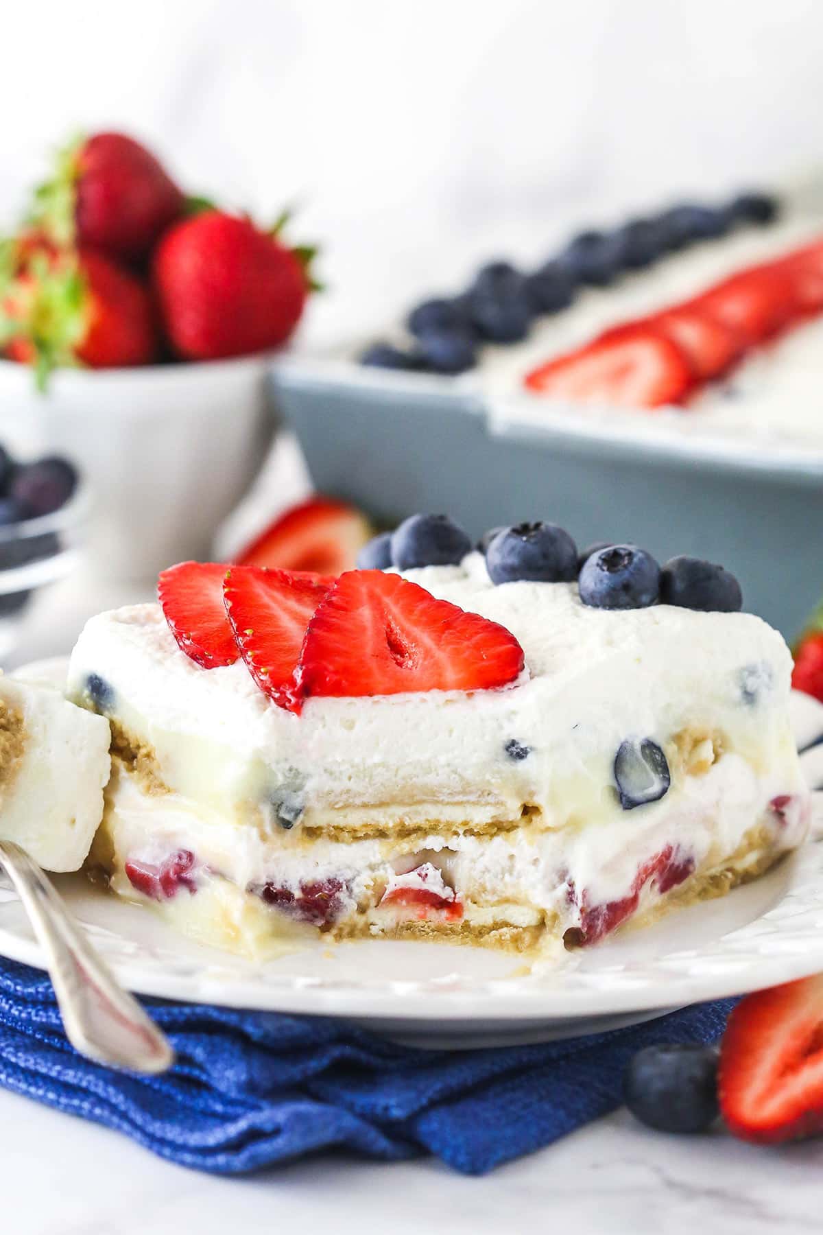 slice of berry icebox cake on white plate with blue napkin underneath with a bit taken out