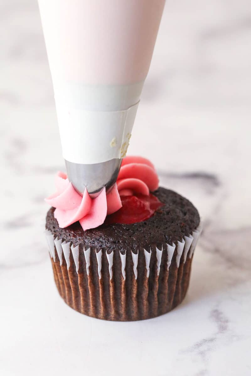 Piping raspberry frosting onto chocolate cupcakes