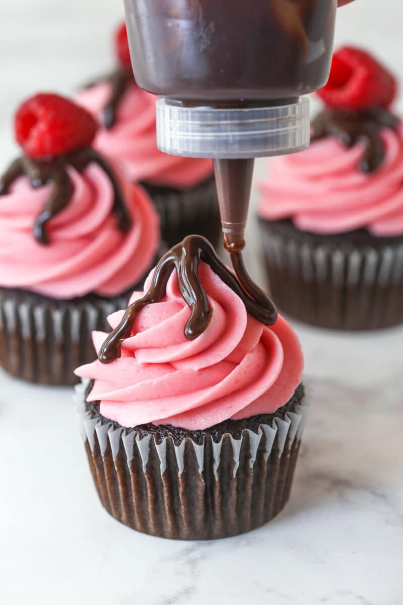 Drizzling ganache over raspberry frosting on cupcakes