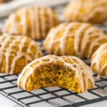 Pumpkin cookies on a cooling rack, one with a bite missing