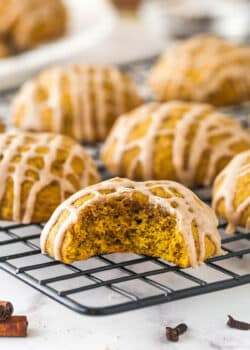 Pumpkin cookies on a cooling rack, one with a bite missing