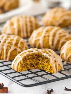 Pumpkin cookies on a cooling rack, one with a bite missing