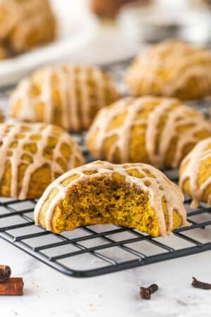 Pumpkin cookies on a cooling rack, one with a bite missing