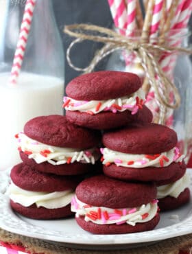 Red Velvet Cookie Sandwiches on white plate stacked with pink, red, white sprinkles