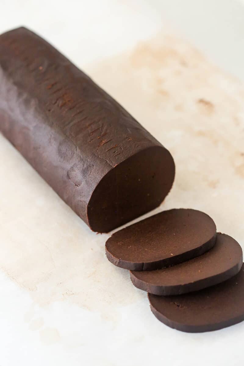 A log of chocolate shortbread cookie dough with a few cookies sliced