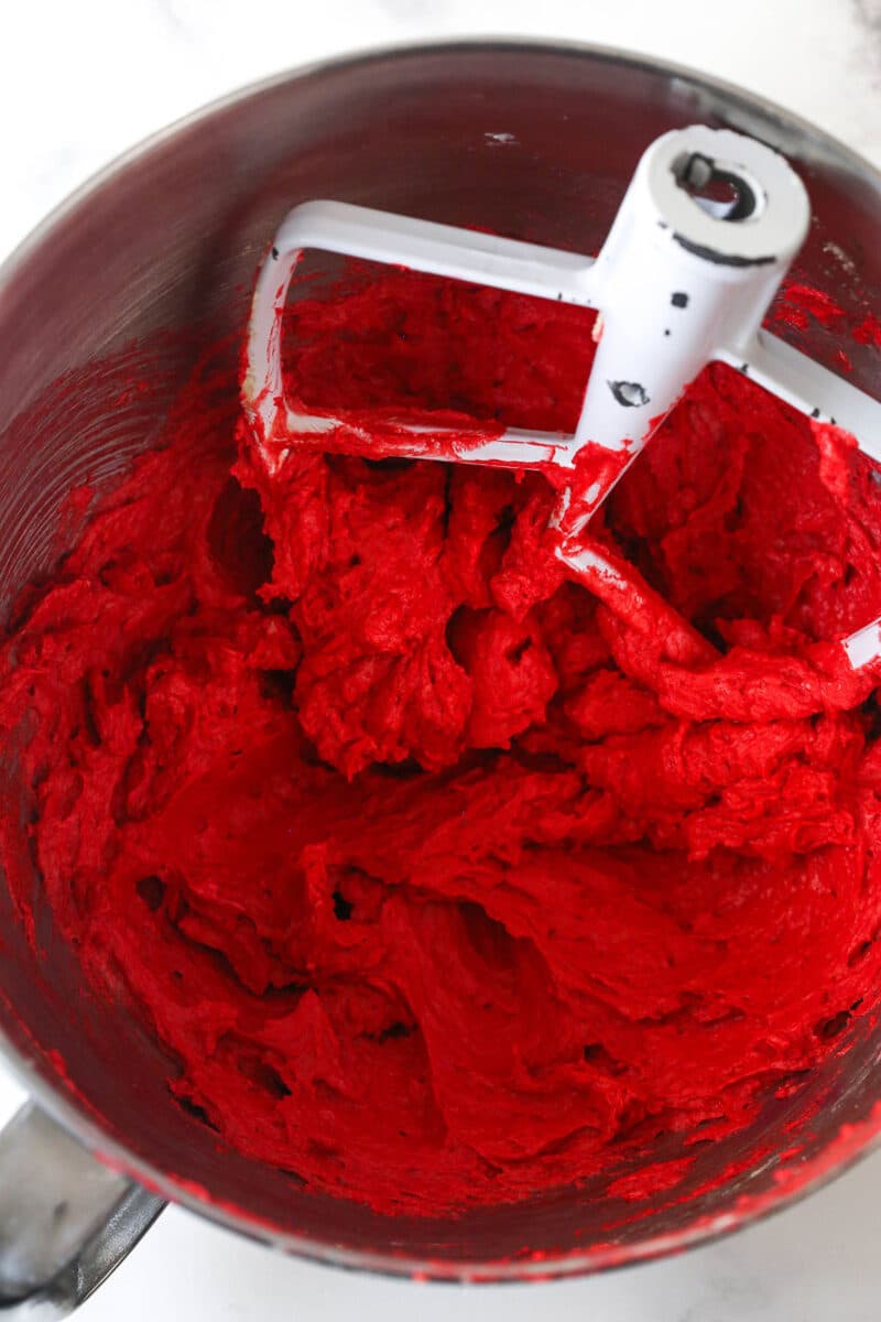 Red food coloring added to creamed butter and sugar in a mixing bowl