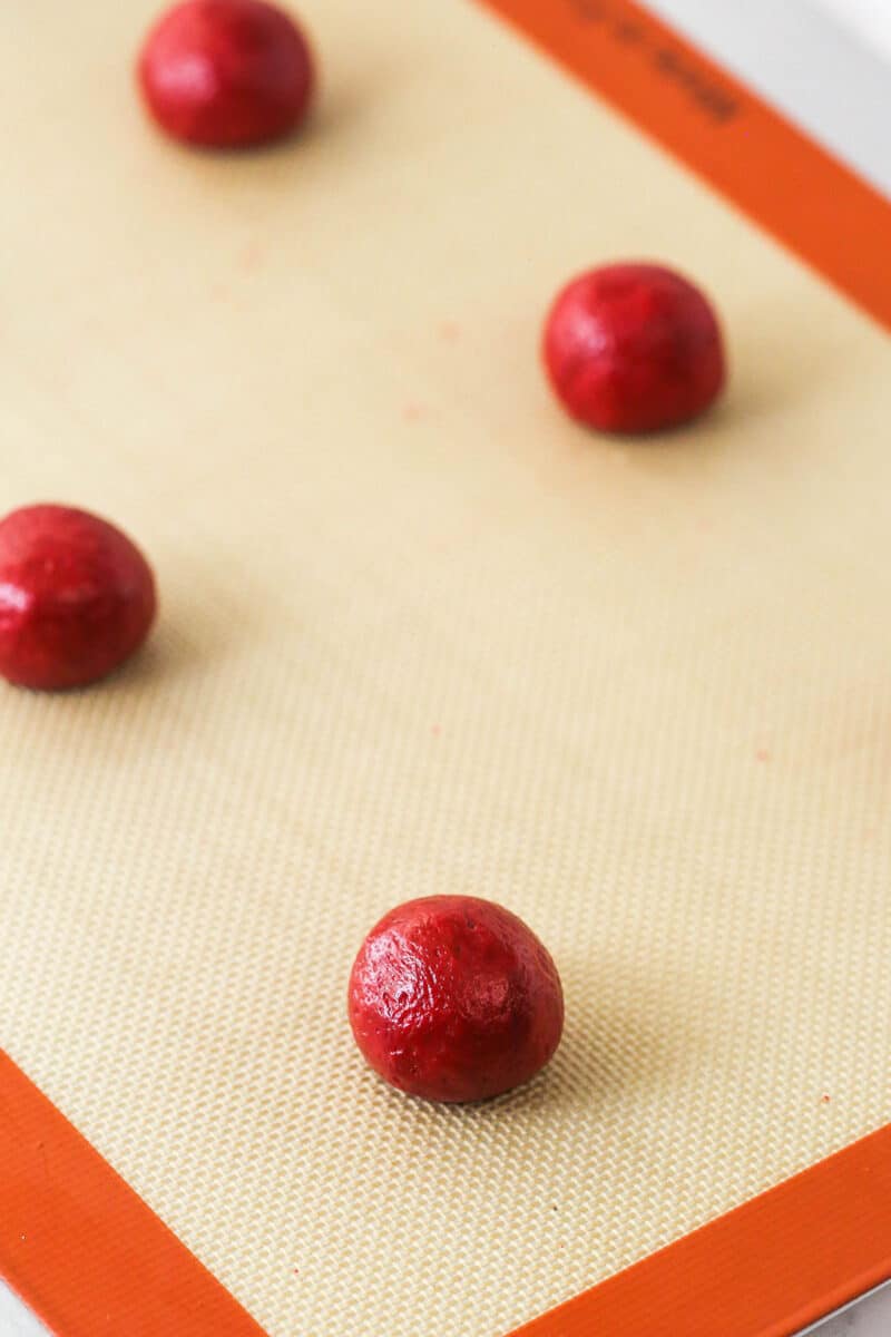 Balls of red velvet cookie dough on a baking sheet