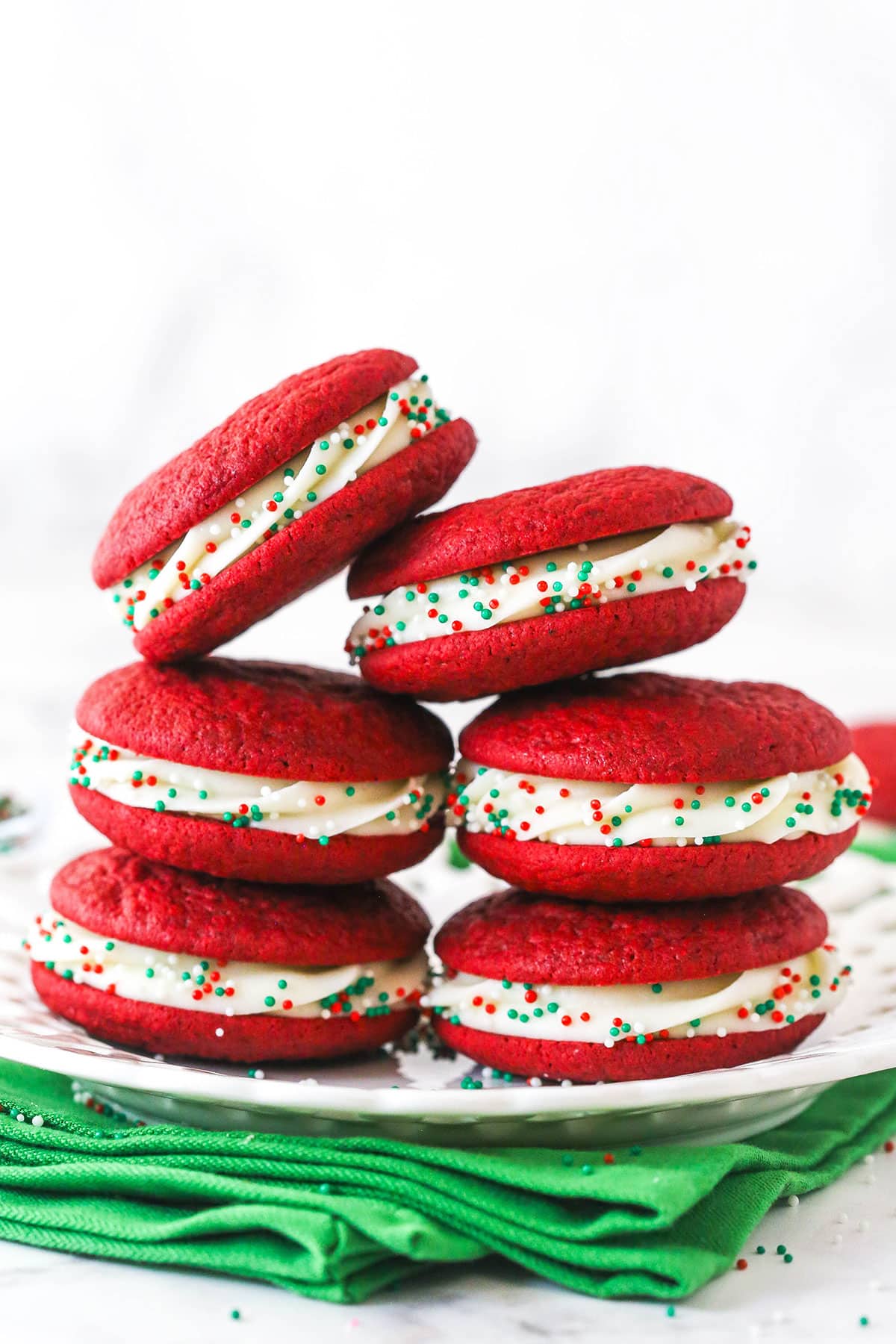 Red velvet cookie sandwiches with green sprinkles stacked on a plate