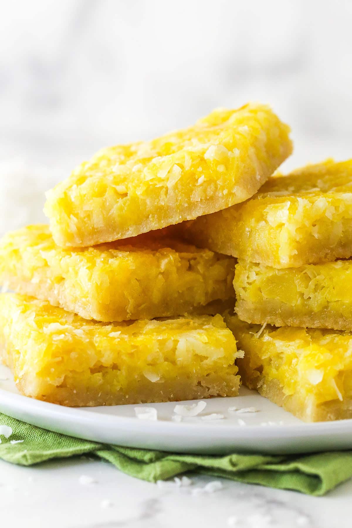 pineapple coconut bars piled onto white plate with green napkin underneath