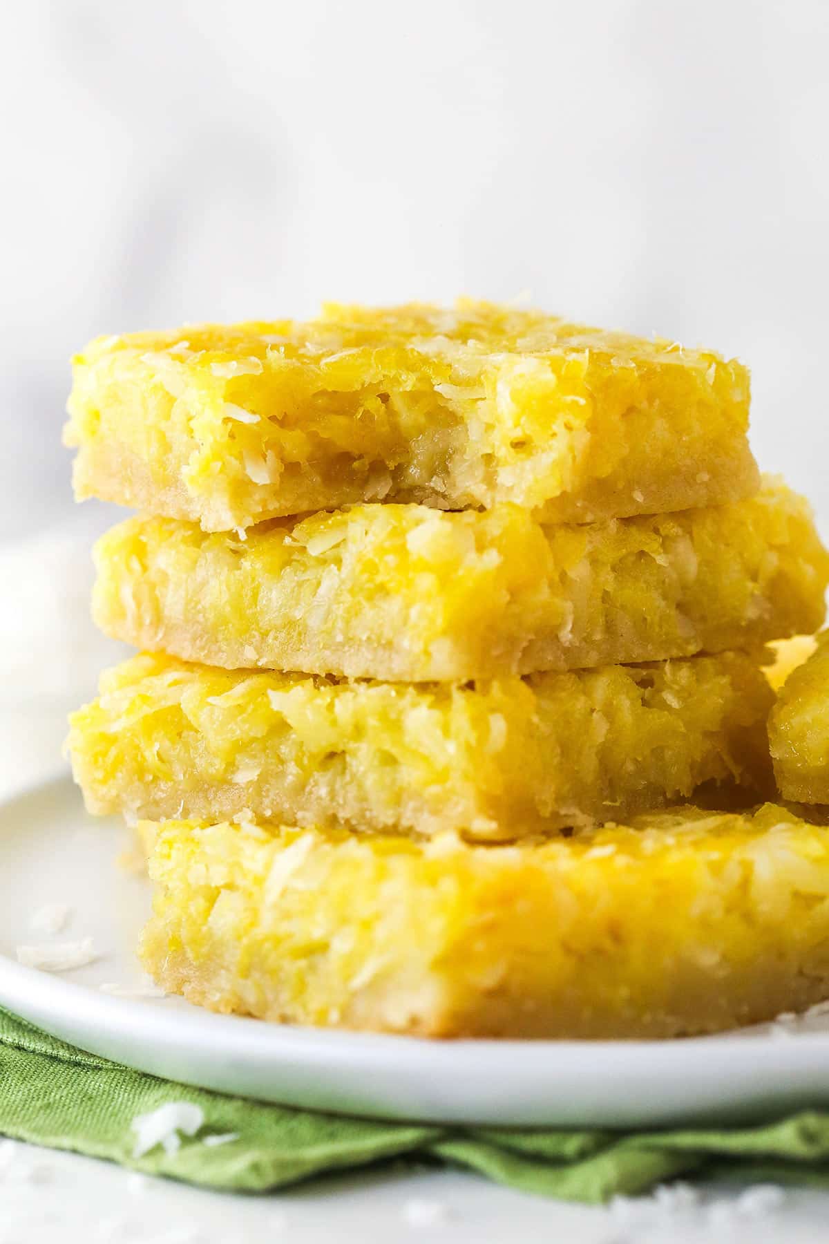 stack of pineapple coconut bars on a plate with a bite taken out of top one