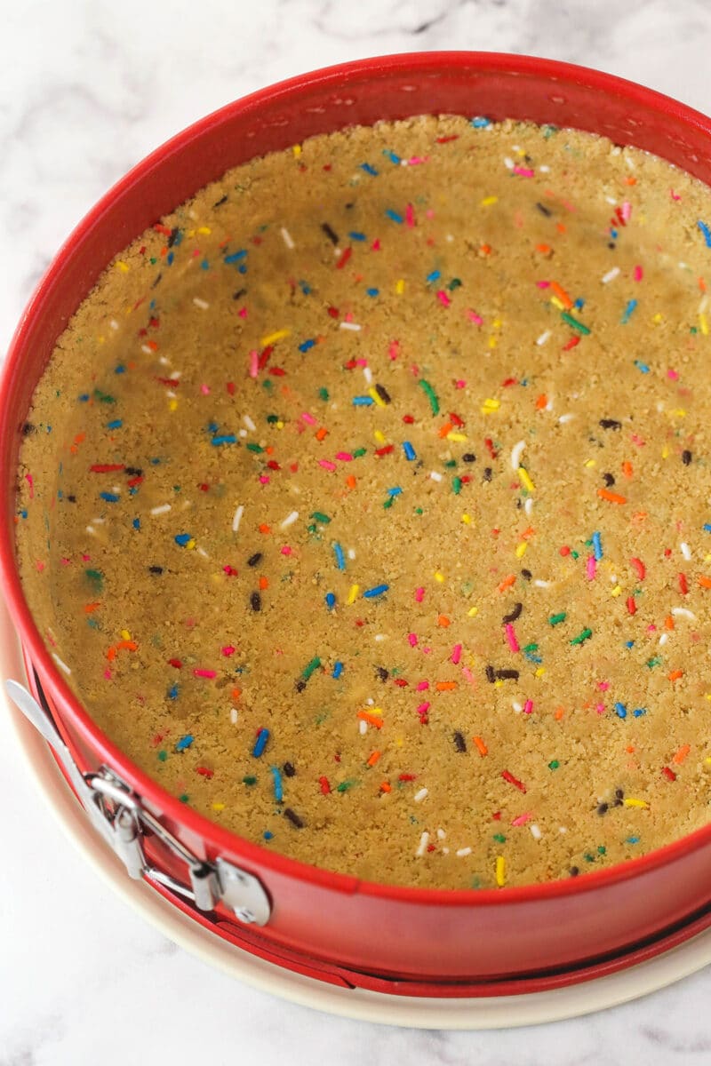 Golden Oreo crust with sprinkles pressed into a springform pan