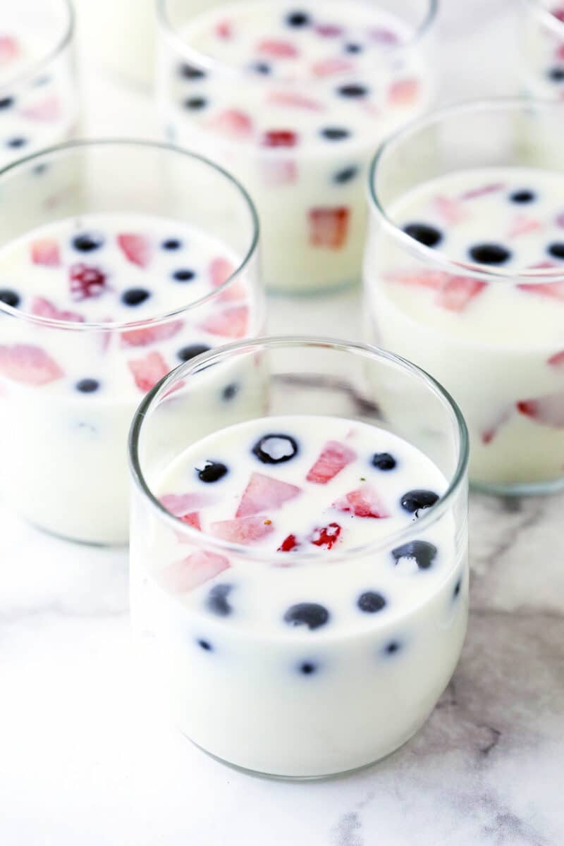 glass cups filled with milk and gelatin mixture and fruit prior to chilling