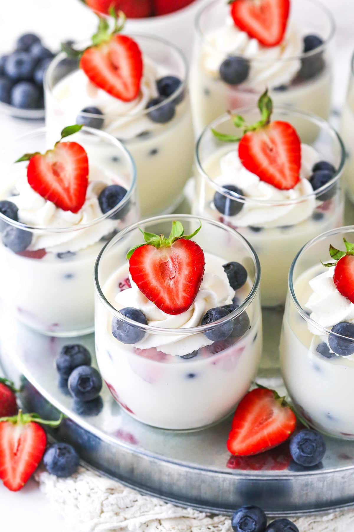overhead image of cups of panna cotta with fresh berries sitting on silver platter with fruit around it
