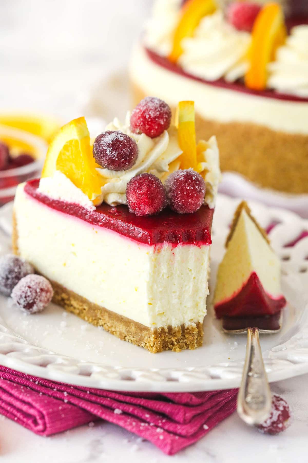 A slice of no bake cranberry orange cheesecake on a plate with a fork with a bite sitting next ot it