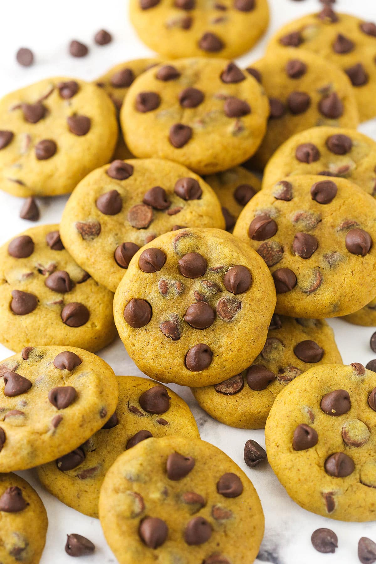 A scattered pile of pumpkin chocolate chip cookies on marble countertop.