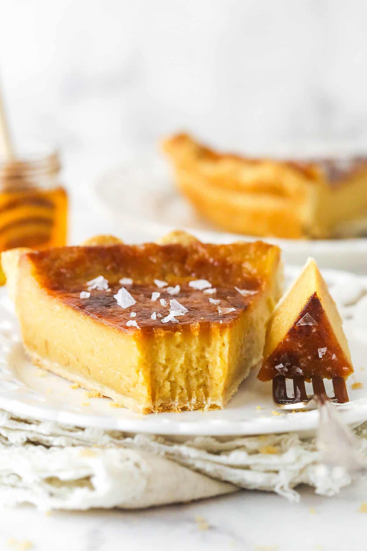 A slice of salted honey pie on a plate, with a bite on a fork