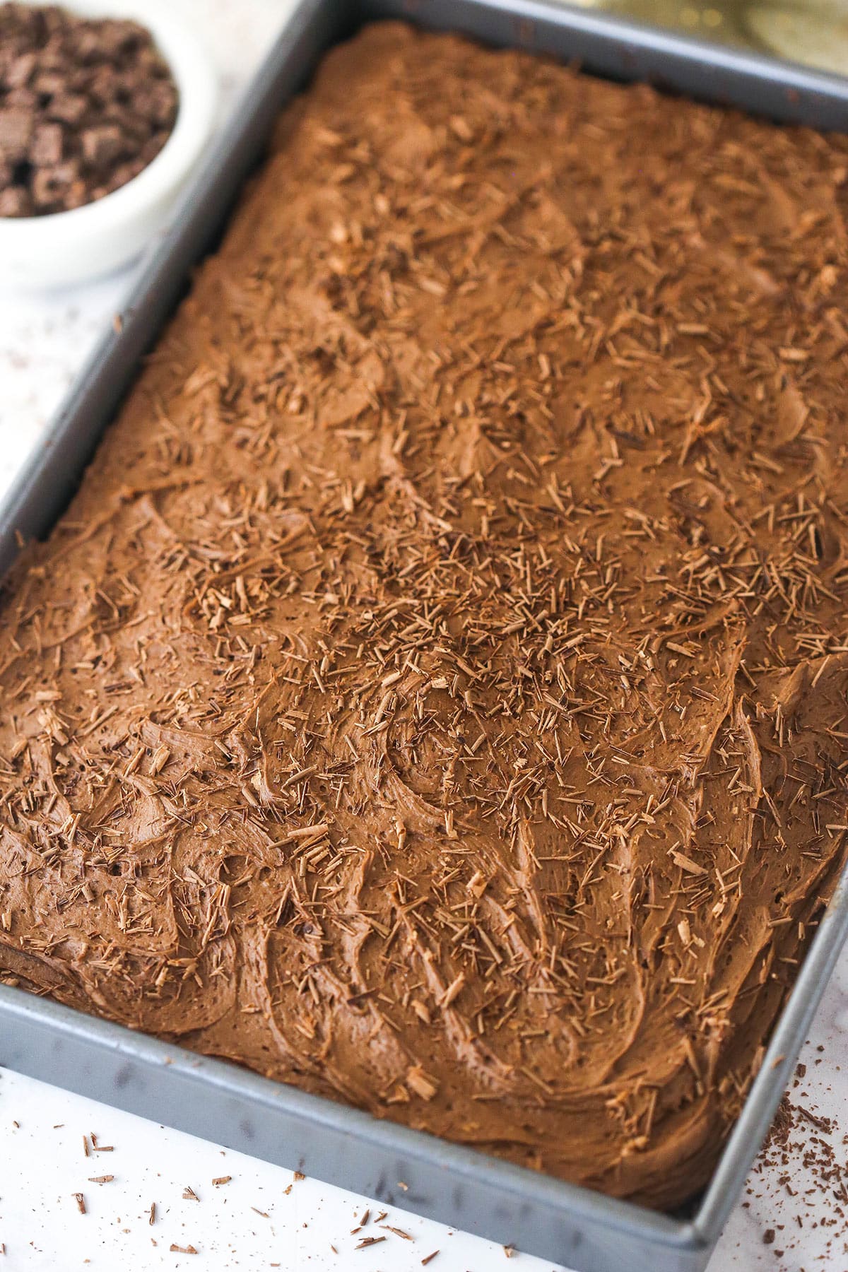 fully frosted chocolate sheet cake in the pan with chocolate shavings on top