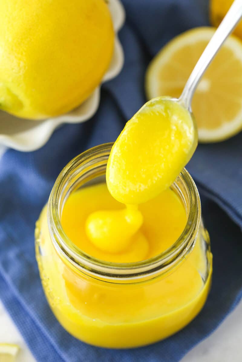 overhead image of lemon curd being drizzled into clear jar with a spoon