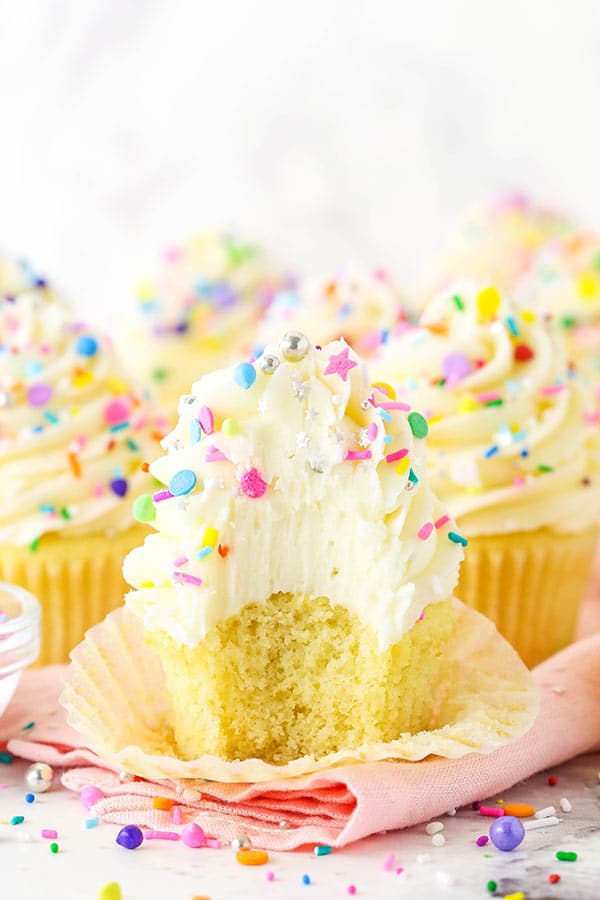 Vanilla cupcake with frosting and sprinkles with a bite taken out of it