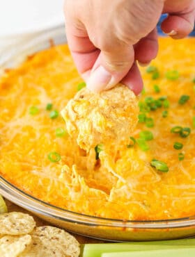 A chip scooping up some Cheesy Buffalo Dip from a clear bowl.