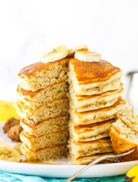 A stack of banana pancakes with one piece missing and slices of bananas on top