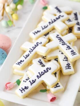 "He Is Risen" Cutout Cookies stacked on a white platter with decorative pink roses