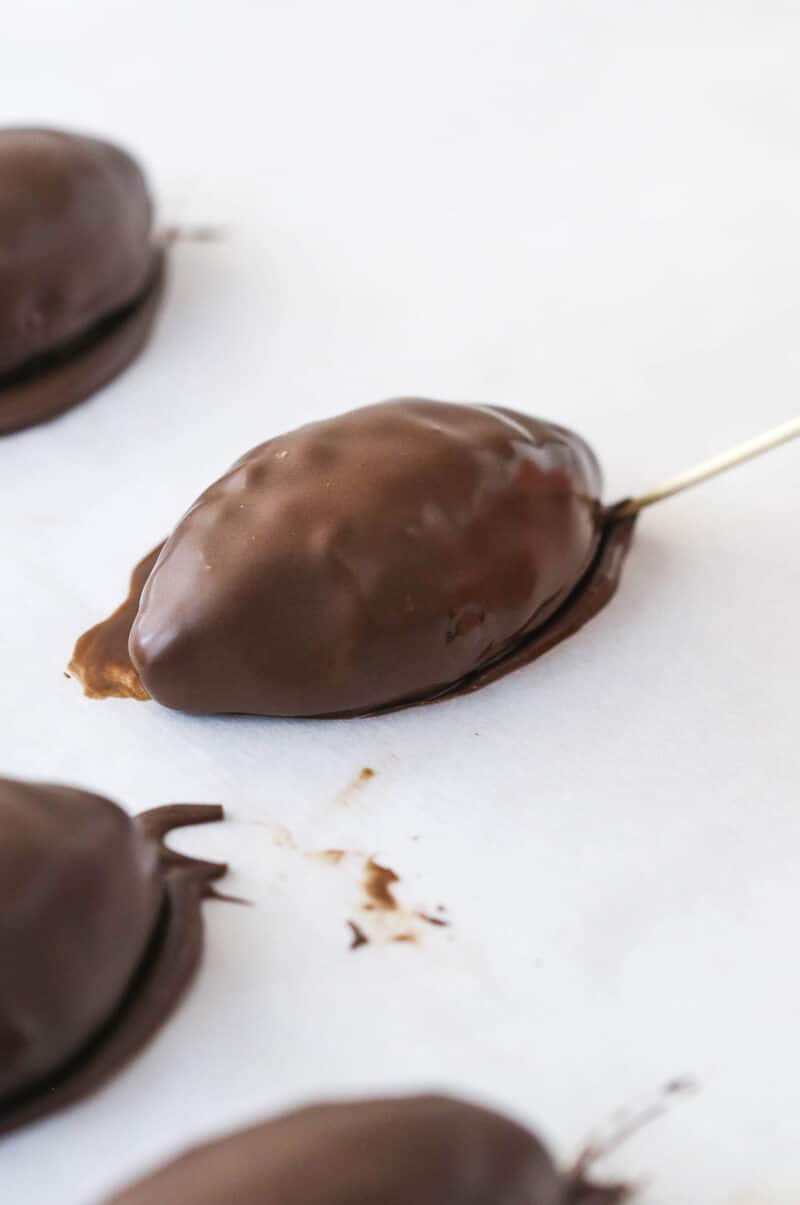 Using a toothpick to draw a line around the base of a chocolate-covered cookie dough football.