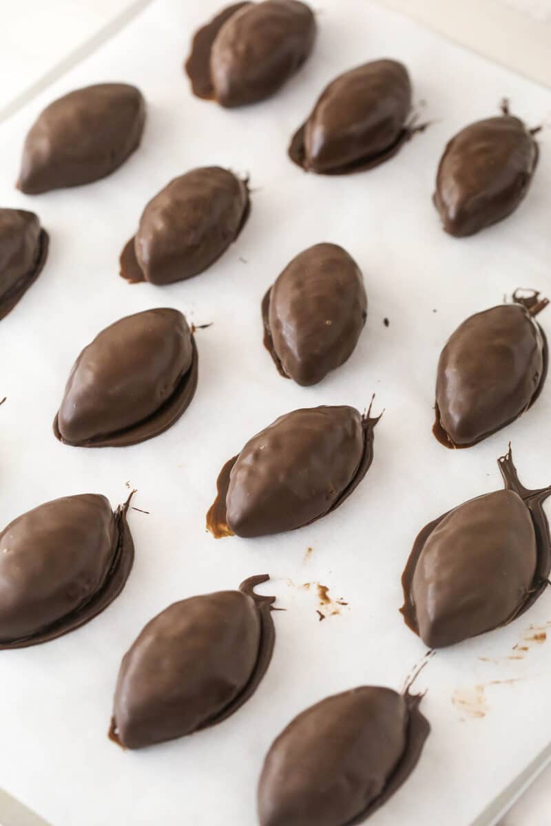 Cookie dough footballs coated in chocolate left to dry on a sheet of parchment paper.