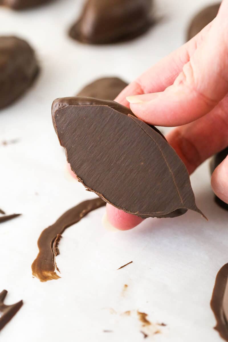 Lifting a chocolate coated cookie dough football off of a sheet of parchment paper.