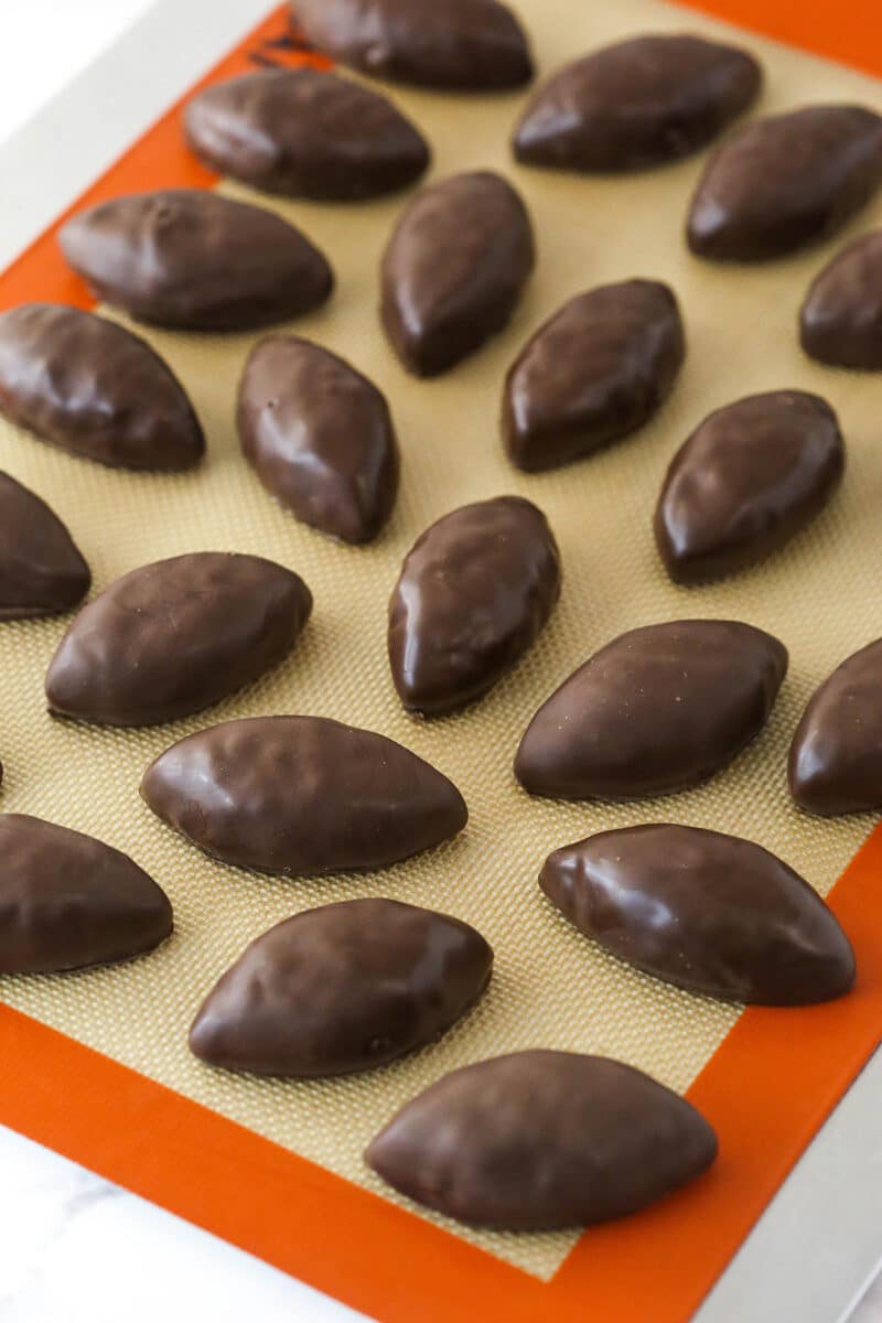 Chocolate-coated cookie dough footballs on a silicon mat.