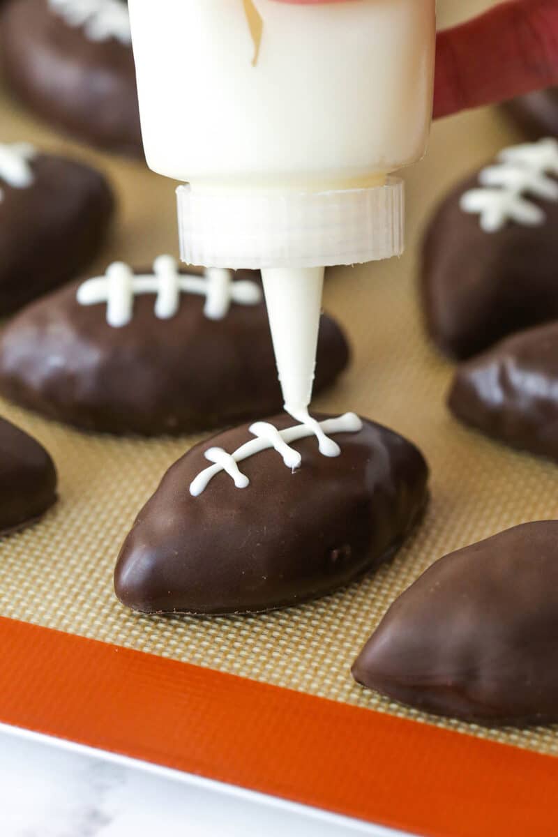 Piping white chocolate laces onto cookie dough footballs.