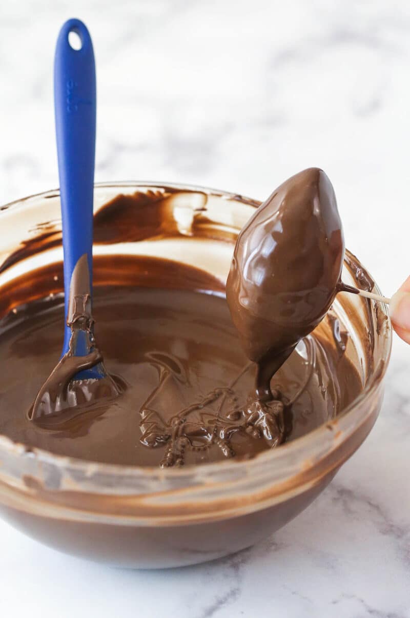 Dipping a cookie dough football in chocolate.