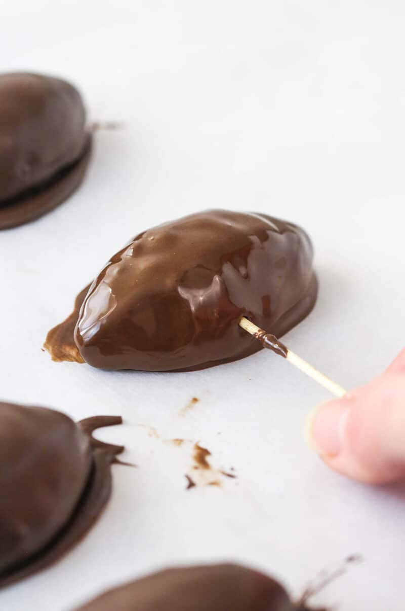 Pulling a toothpick out of a chocolate-coated cookie dough football.