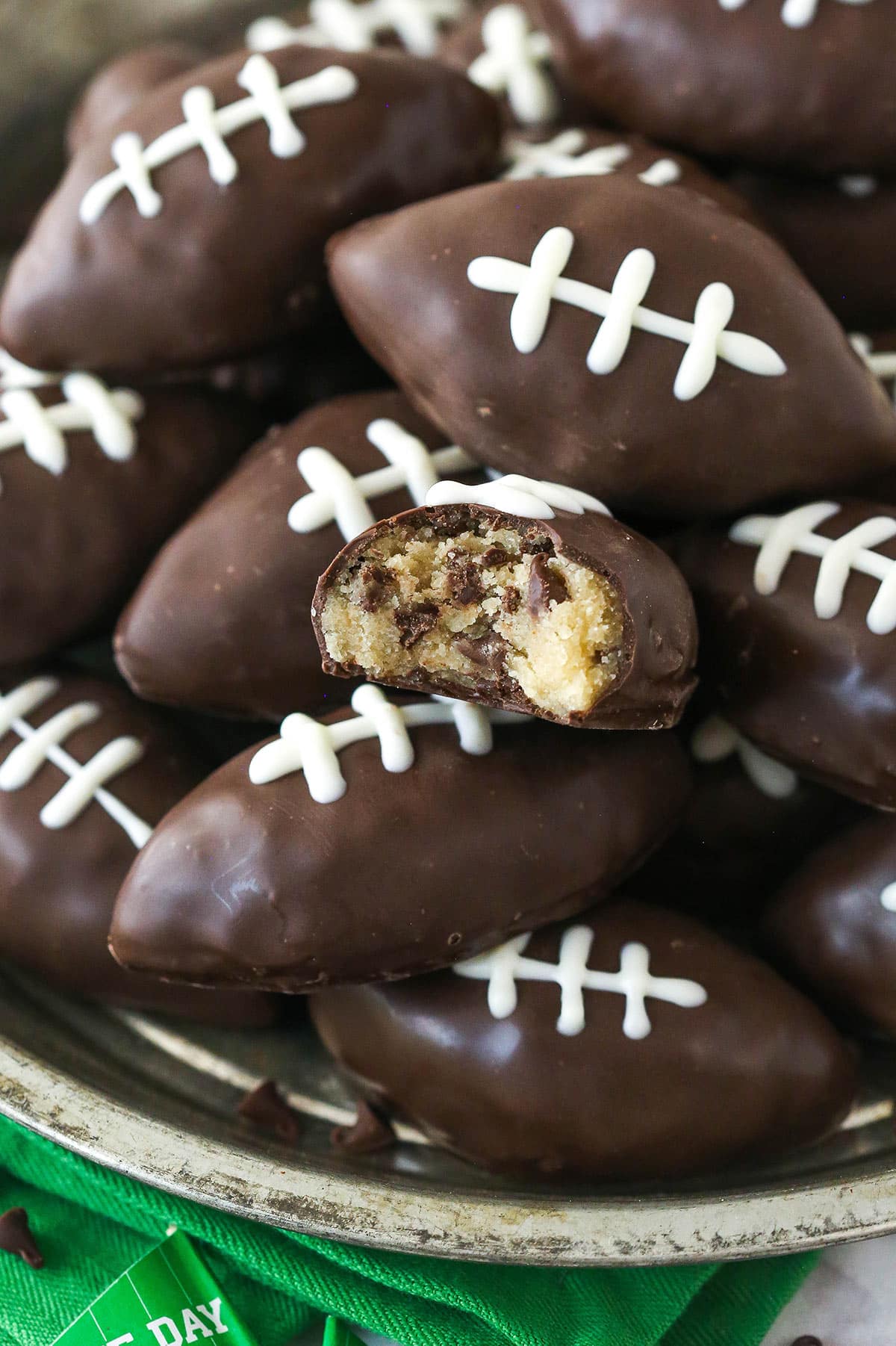 Cookie dough footballs on a serving plate. One has a bite take out of it.