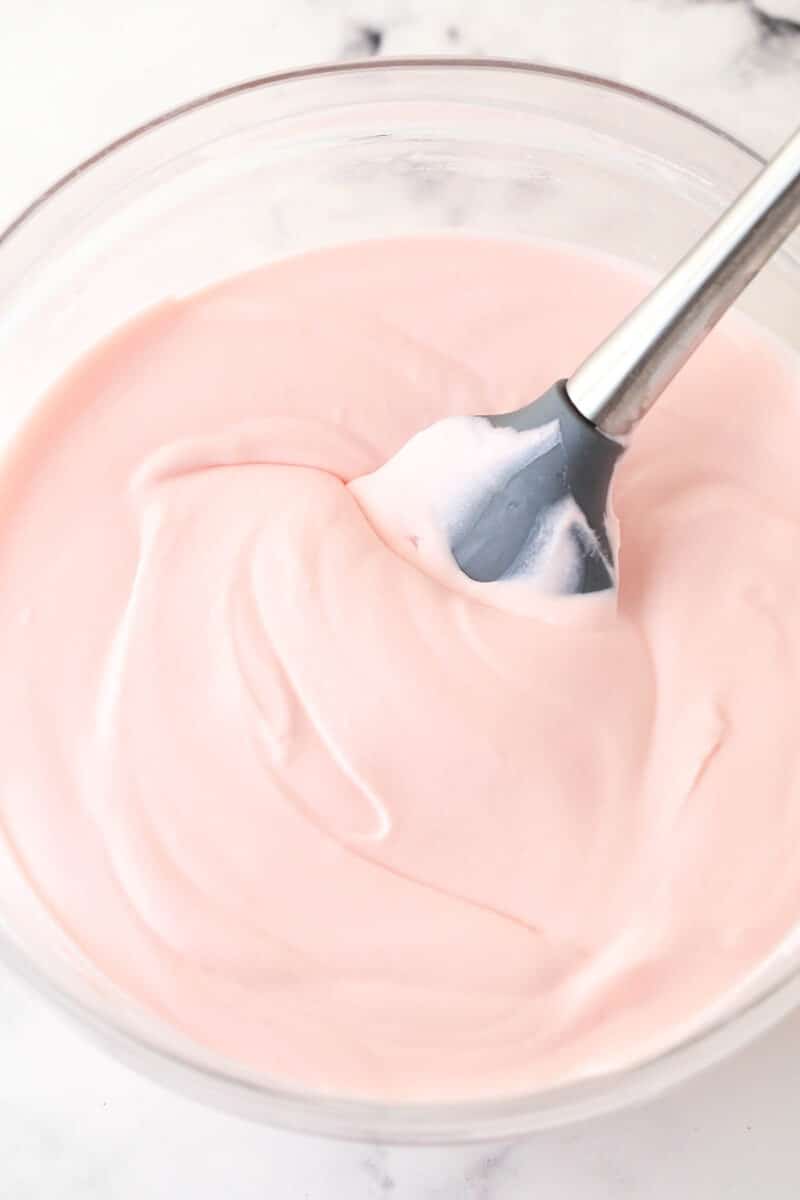 Folding whipped cream into sweetened condensed milk and maraschino cherry juice.