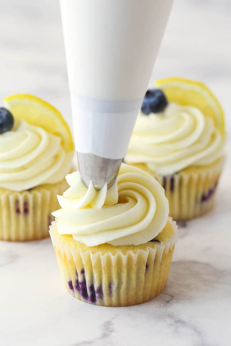 Piping lemon cream cheese frosting onto a lemon blueberry cupcake.