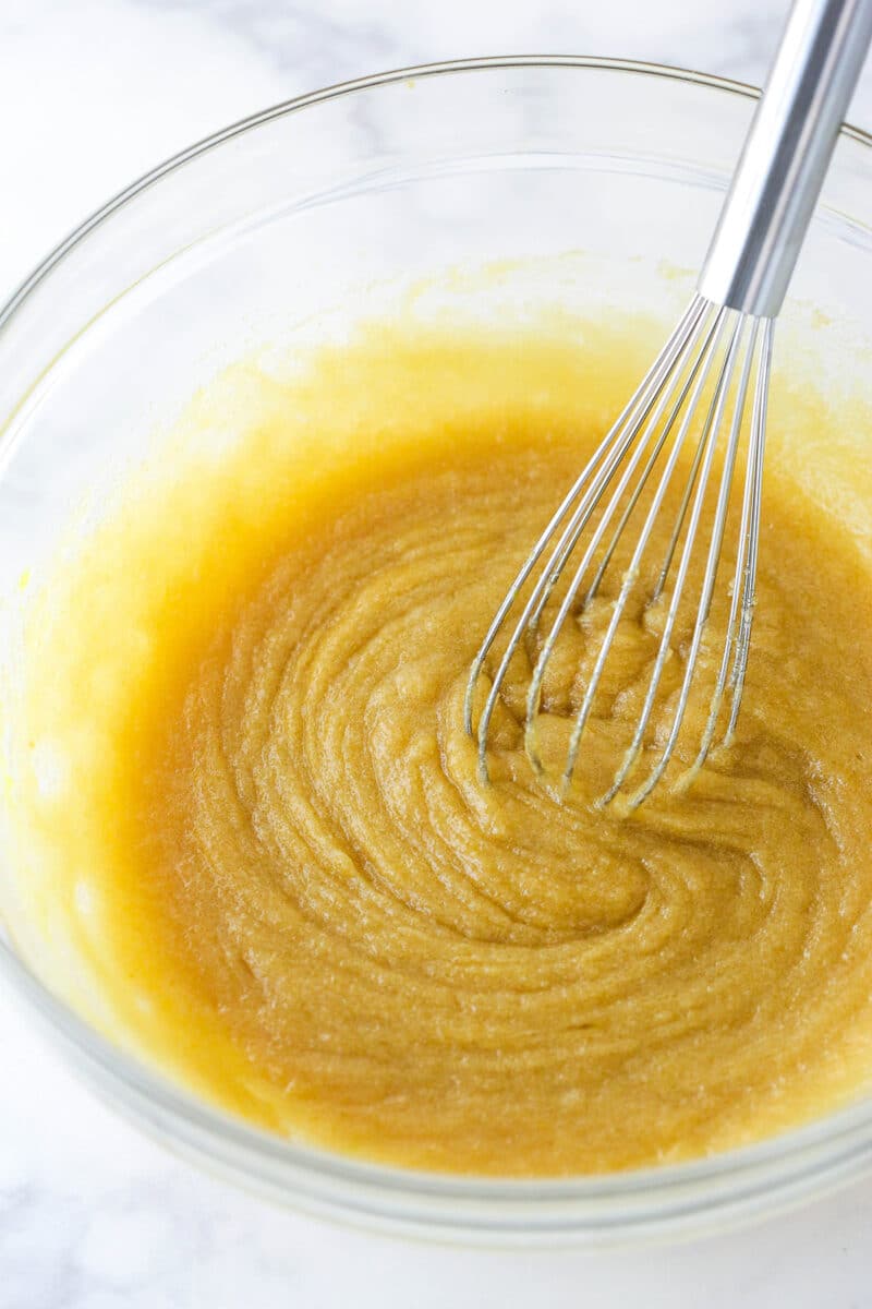 Whisking an egg and vanilla into melted butter and sugar.