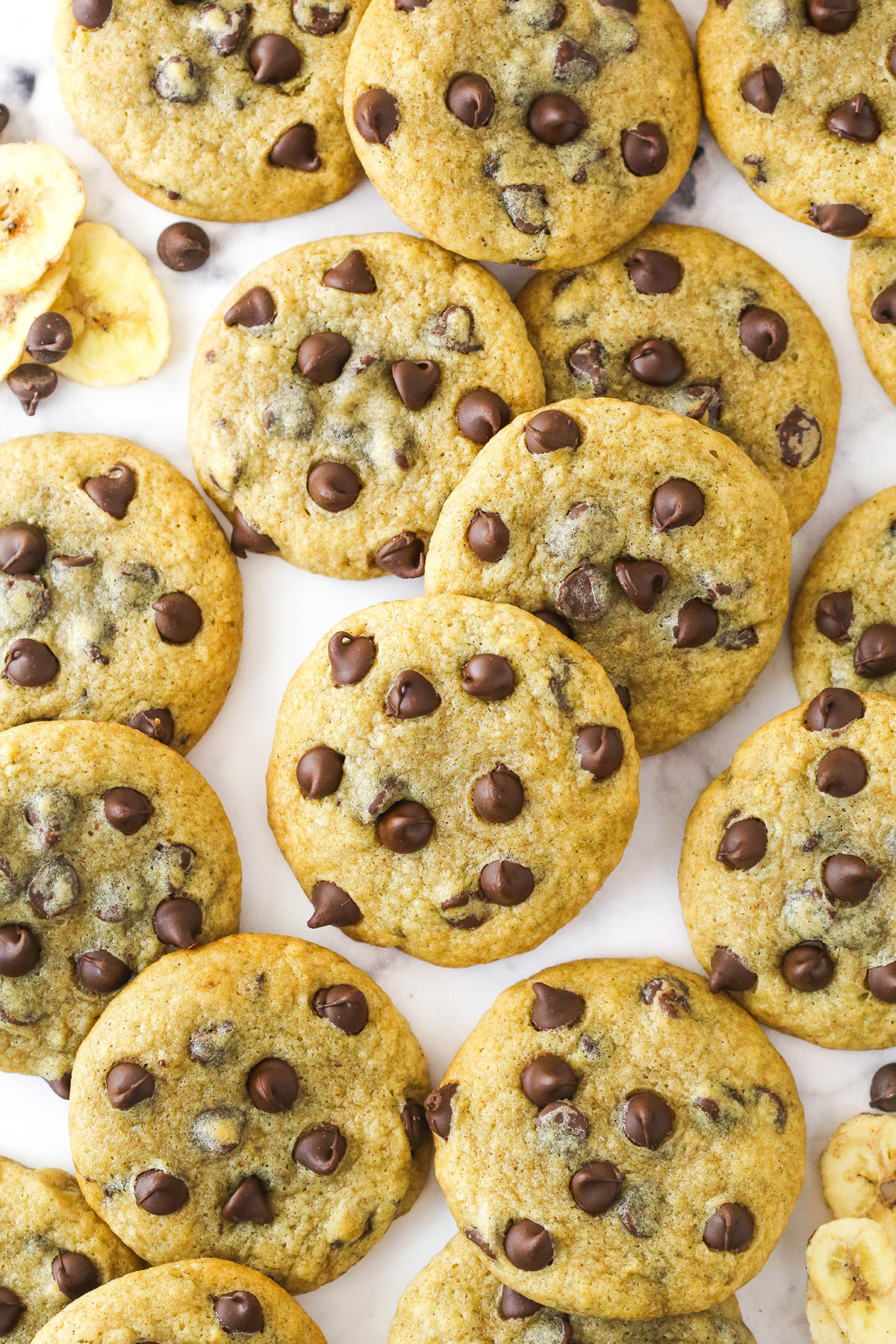 Overhead image of banana chocolate chip cookies scattered on a countertop.