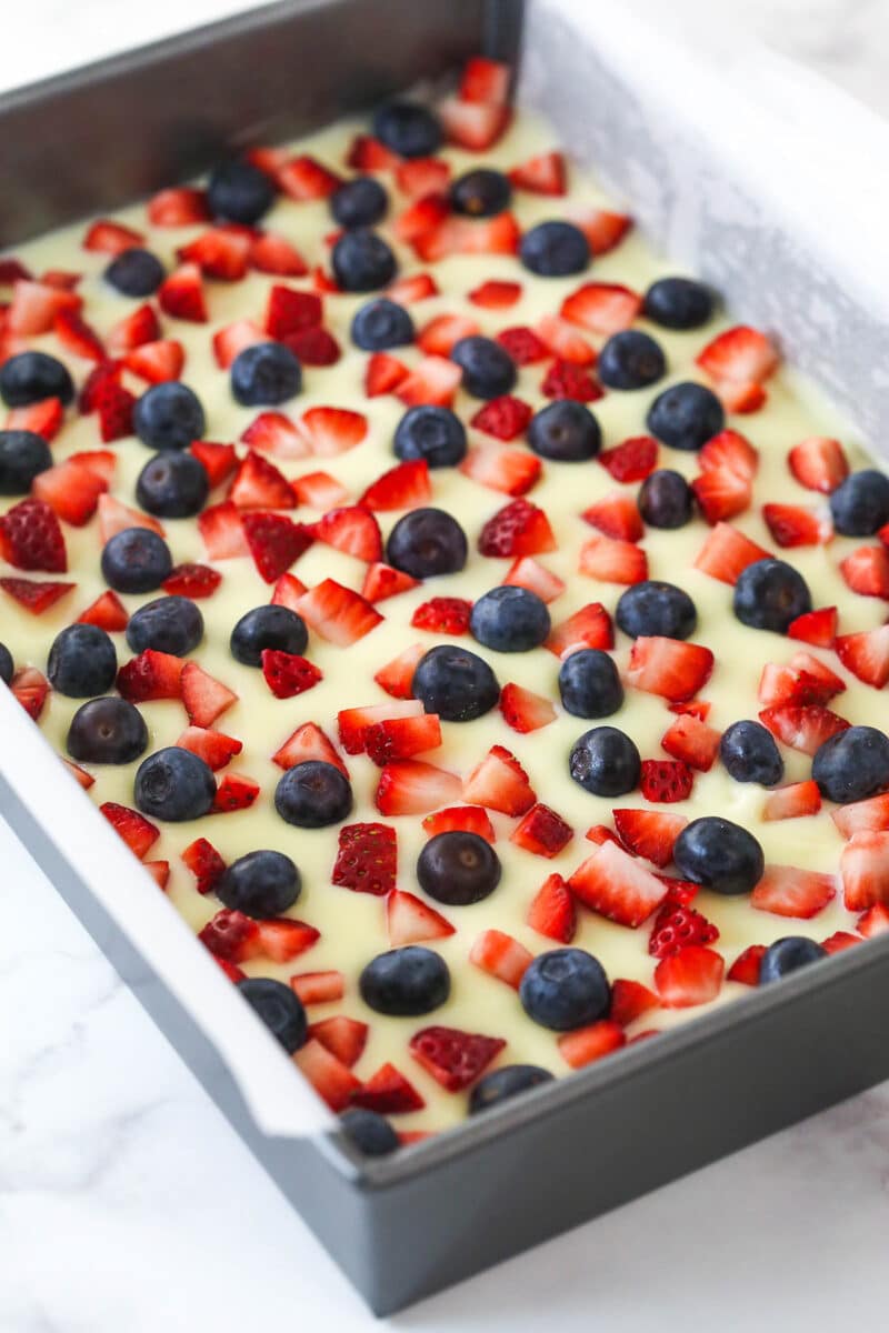 Topping a layer of oatmeal cookie dough with cheesecake filling and fresh berries.