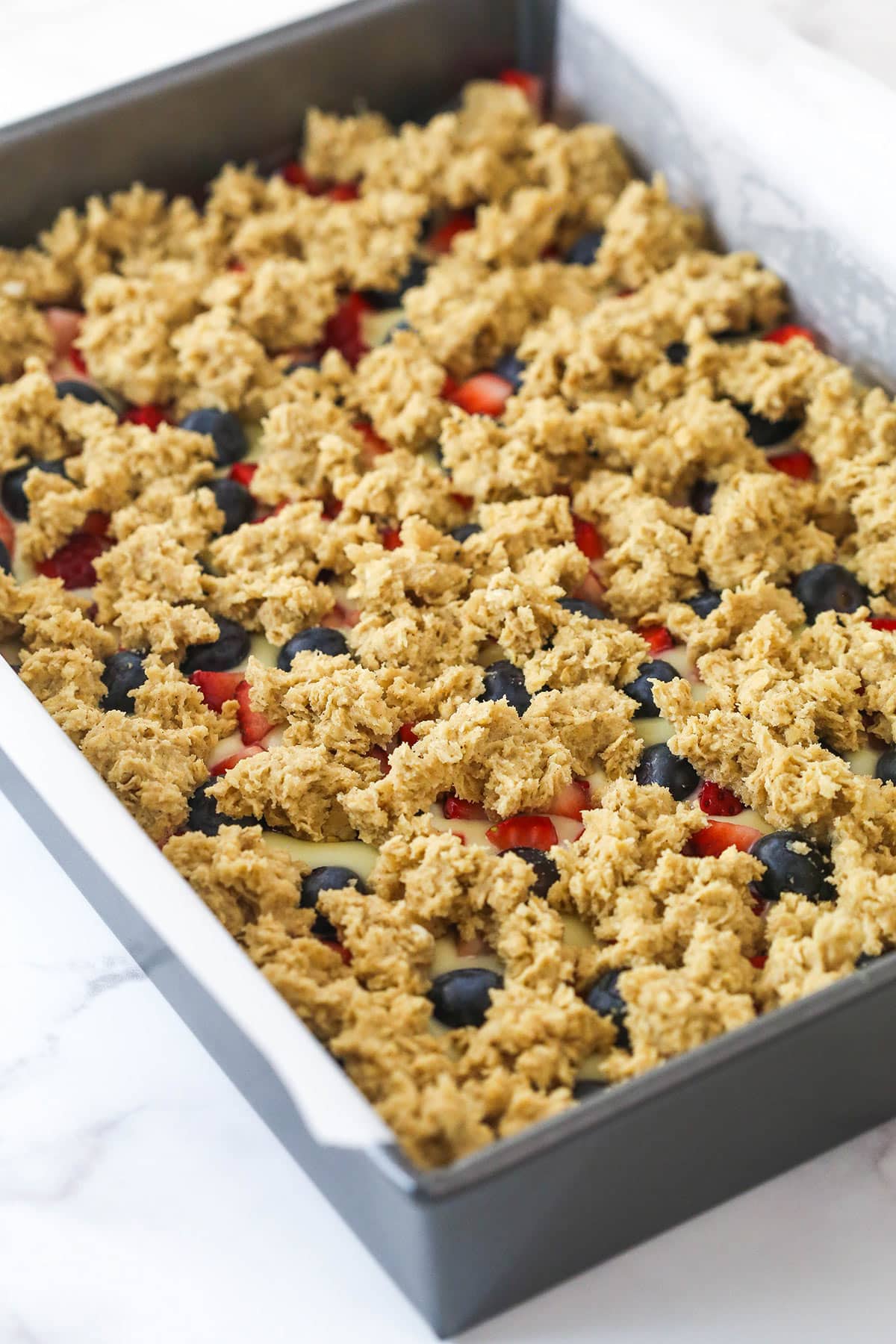 Sprinkling crumbled oatmeal cookie dough on top the cheesecake filling for berry oatmeal cheesecake bars.