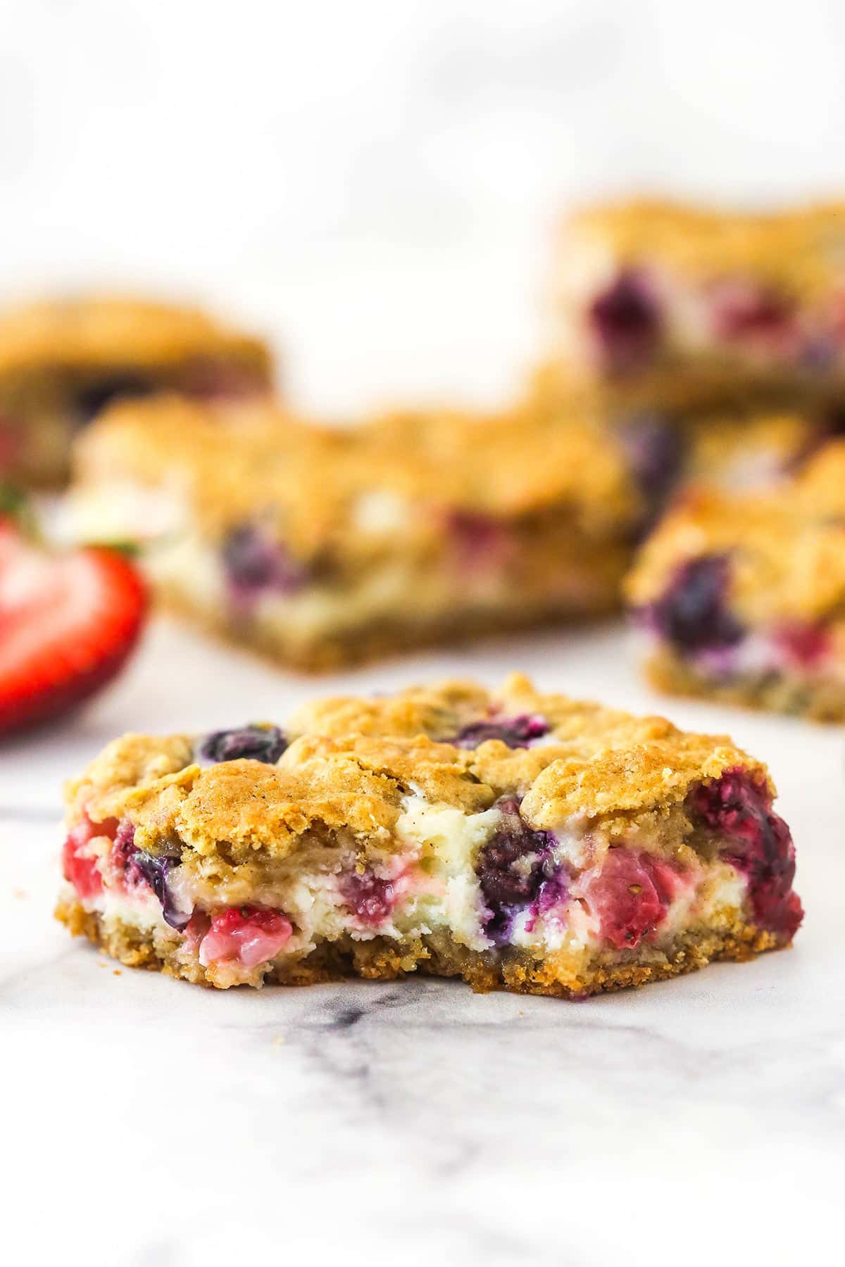 A berry oatmeal cheesecake bar on a countertop with a bite taken out of it.