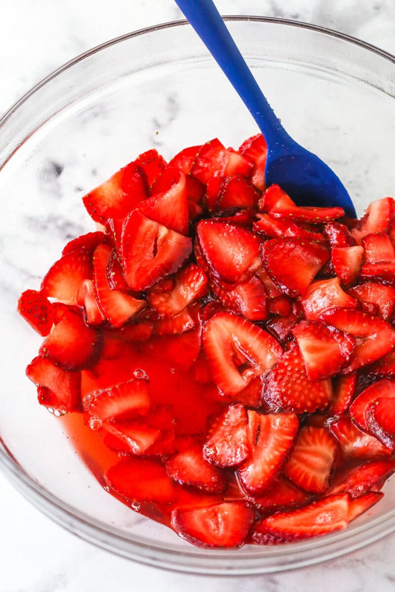 Strawberries coated in sugar in a bowl, releasing their juices.